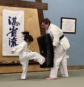 young girl kicking into a pad held by a teacher